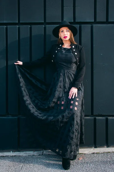 Açık tenli, sarı saçlı, uzun siyah elbiseli, siyah boğa güreşçisi ve siyah bir duvara poz veren genç bir kadınla moda fotoğrafı..