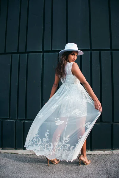 Kahverengi tenli, siyah saçlı, gümüş elbiseli, beyaz ceketli ve siyah arka planda şapkası olan genç bir kadınla moda fotoğrafçılığı..