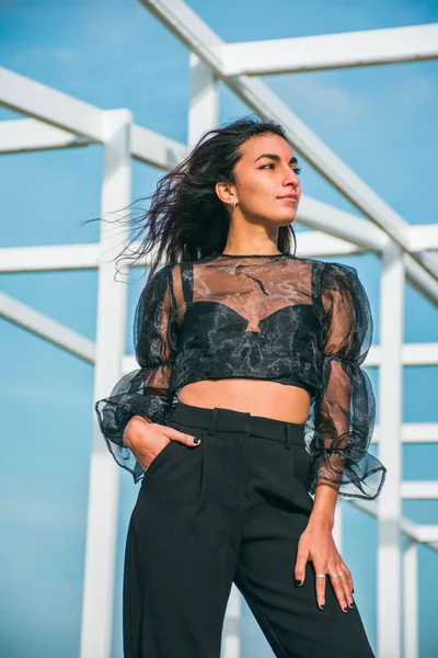Siyah elbiseli genç esmer bir kadınla moda fotoğrafçılığı. Gündüz vakti bazı beyaz binaların önünde poz veriyorlar..