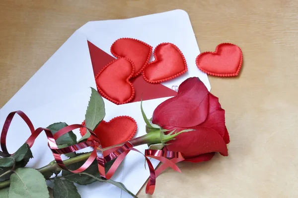 Kuvert med kort och hjärtan, röd ros med dekorband är på bordet. Utsikten från toppen — Stockfoto