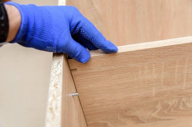 Ahşap mobilya montajı sırasında koruyucu eldivenli bir zanaatkar. Ev onarım konseptleri. Orta yoğunluklu fiber ahşap ürün. Mobilya fikirleri.