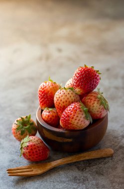 İğne rengi arka planda ahşap kasede taze çilekler.