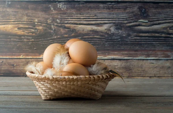 Farm fresh eggs in a basket on a wooden table. There is a wooden background.