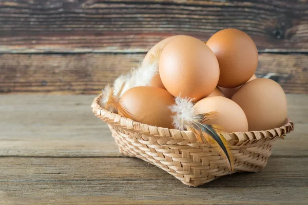 Farm fresh eggs in a basket on a wooden table. There is a wooden background.