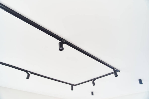 Modern LED black track spot lights in the interior. Hanging lamps spotlights attached to a concrete ceiling in an office loft room