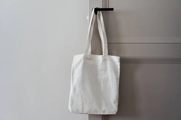 White eco friendly bag hanging on the door handle. Canvas tote bag