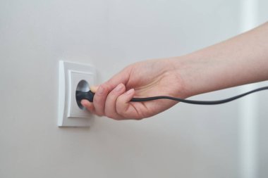 Genç bir kız prizin fişini takıyor. Genç kadın şarj aletini prize takıyor. Yüksek kalite fotoğraf