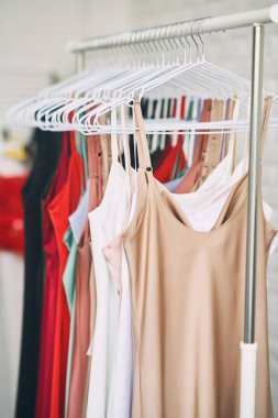 Çok renkli elbiseler mağazadaki askılarda asılı. Kadın elbiseleri satışı. Değişik renkte kadın kıyafetleri asılı..