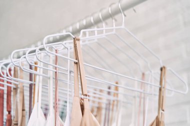 Çok renkli elbiseler mağazadaki askılarda asılı. Kadın elbiseleri satışı. Değişik renkte kadın kıyafetleri asılı..