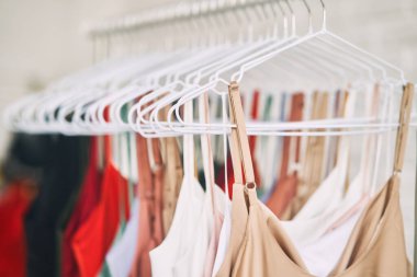 Çok renkli elbiseler mağazadaki askılarda asılı. Kadın elbiseleri satışı. Değişik renkte kadın kıyafetleri asılı..