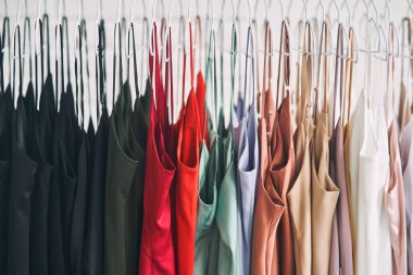 Çok renkli elbiseler mağazadaki askılarda asılı. Kadın elbiseleri satışı. Değişik renkte kadın kıyafetleri asılı..