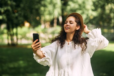 Şapkalı güzel bir kız parkta telefonuyla selfie çekiyor. Yüksek kalite fotoğraf