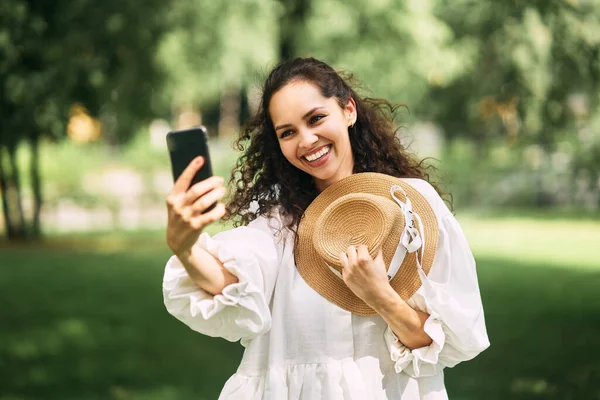 帽子をかぶった若い美しい女の子が公園で彼女の電話で自撮りをします 高品質の写真 — ストック写真