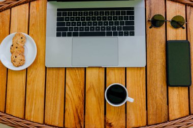Düz yatıyordu. Çalışma alanı, gri modern dizüstü bilgisayar ve akıllı telefon ile doğal ahşap kahverengi ofis masasında çalışmak üzere minimalist konsept. Kahve molası, bir fincan kahve ve masada kurabiyeler. Boşluğu kopyala