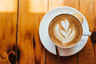 Düz yatıyordu. Hafif bir kafedeki ahşap bir masada köpüklü bir fincan aromatik kapuçino. Kahve köpüğünde güzel bir desen var. Boşluğu kopyala