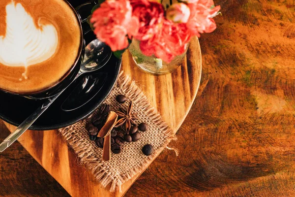 Cappuccino i en svart kopp. Blommor på bordet Royaltyfria Stockfoton