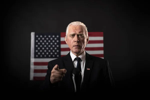 American presidential elections 2020 on a dark background with an American flag, a mature gray-haired man, a character, an actor, a democrat who emotionally gestures and points a finger in a debate.