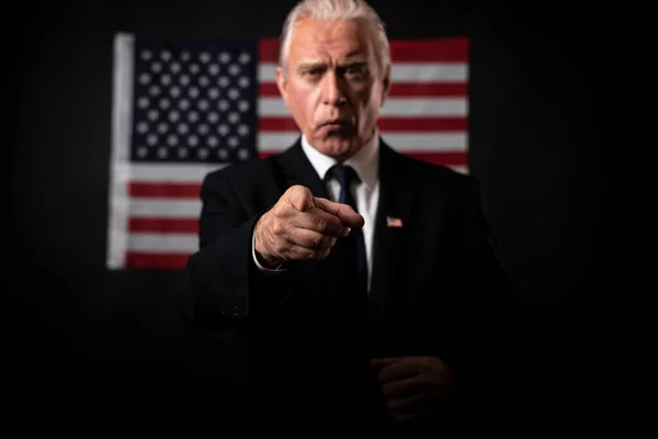 American presidential elections 2020 on a dark background with an American flag, a mature gray-haired man, a character, an actor, a democrat who emotionally gestures and points a finger in a debate.