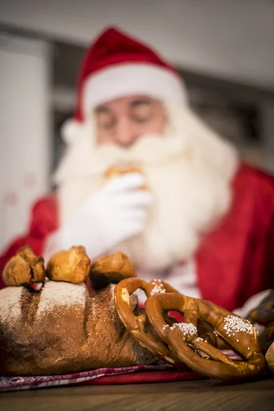 Santa Claus in the kitchen treats tasty buns — Stock Photo, Image
