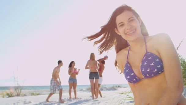 Девушка сидит на пляже, пока друзья играют в мяч — стоковое видео