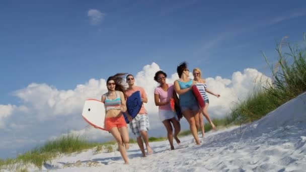 Adolescenti che trasportano assi di corpo attraverso la spiaggia — Video Stock