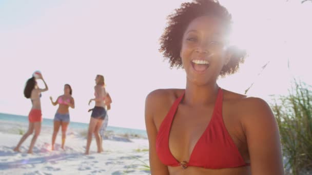 Meisje, zittend op het strand terwijl vrienden bal spelen — Stockvideo