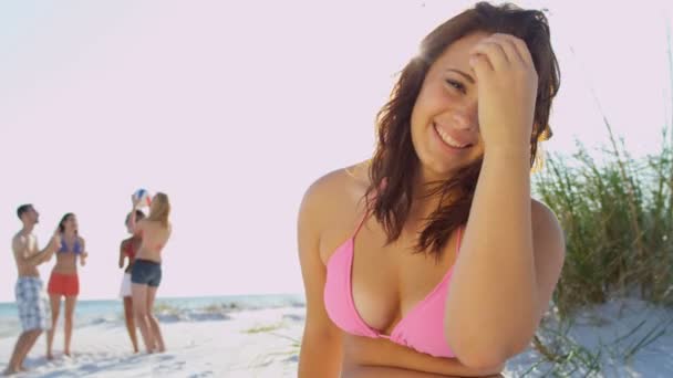 Девушка сидит на пляже, пока друзья играют в мяч — стоковое видео