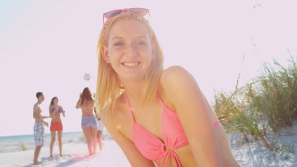 Chica sentada en la playa mientras sus amigos juegan pelota — Vídeos de Stock