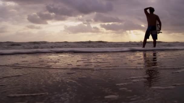 Серфер на пляже наблюдает за волнами — стоковое видео