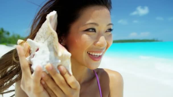 Chinese girl holding seashell on tropical beach — Stock Video