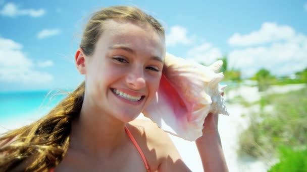 Bir deniz kabuğu kabuk tutan bir plajda genç kız — Stok video
