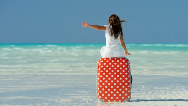 Liten flicka på en strand som sitter på en resväska — Stockvideo