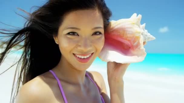 Китаянка держит ракушку на тропическом пляже — стоковое видео