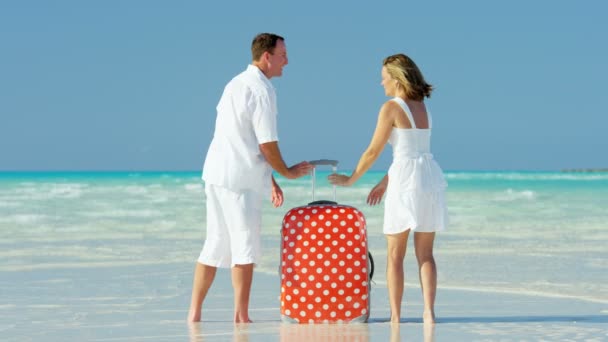 Casal caucasiano em uma praia tropical com mala — Vídeo de Stock