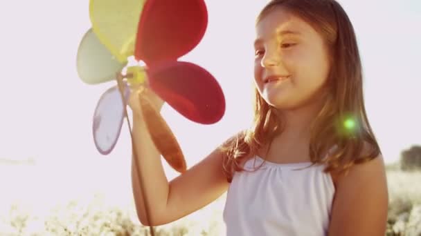 Маленька дівчинка на лузі грає з іграшкою вітряка — стокове відео