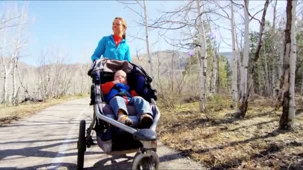 Moeder met zoon in kinderwagen genieten van wandeling in park — Stockvideo