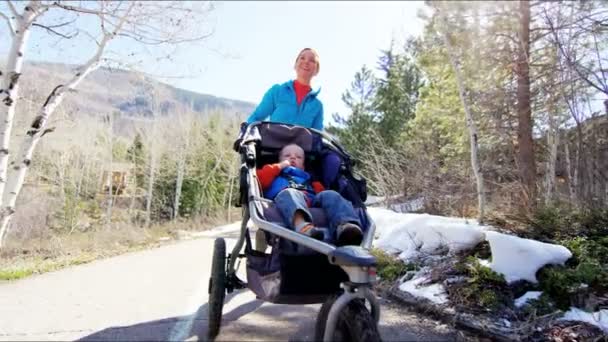 Mãe com filho na cadeira de empurrão curtindo andar no parque — Vídeo de Stock