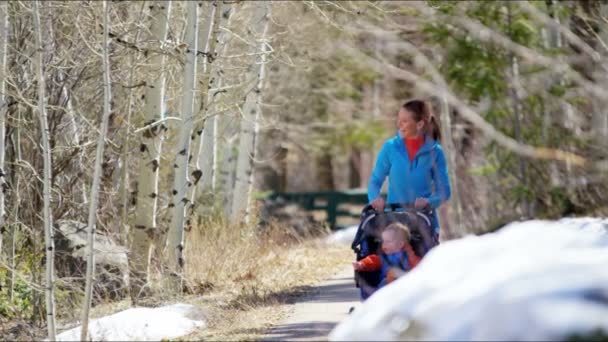 Mãe com filho na cadeira de empurrão curtindo andar no parque — Vídeo de Stock