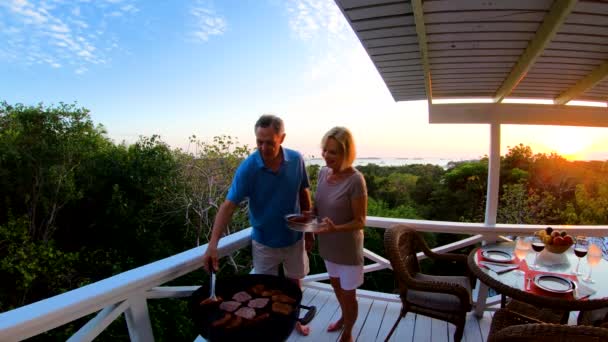 Pareja jubilada cocinando barbacoa en la terraza al atardecer — Vídeo de stock