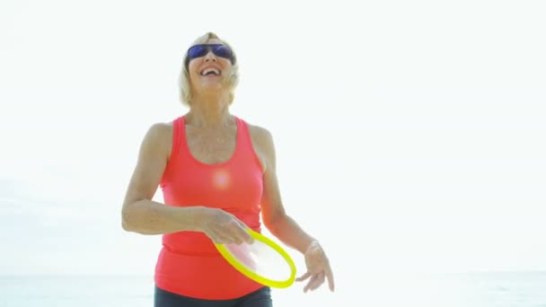 Śmiejąc się starsza Amerykanka gra Frisbee na wybrzeżu — Wideo stockowe