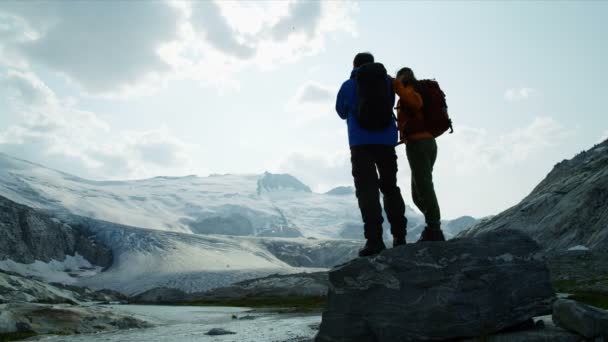 湖の景色氷河の近くの風光明媚な山の中で写真を撮る男性と女性の白人旅行者ハイキング — ストック動画