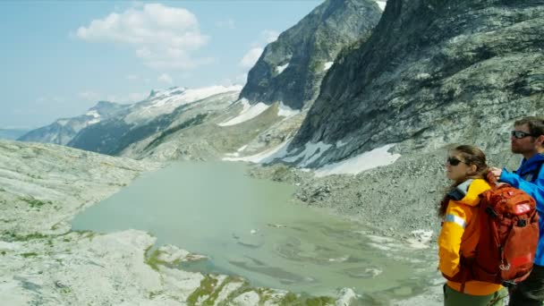 在加拿大高山上冰川湖水瀑布附近观赏风景的白人男女徒步旅行者 — 图库视频影像