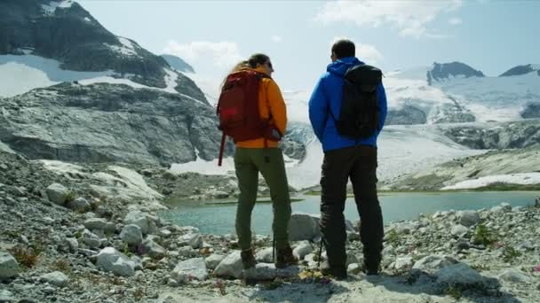 カナダの夏の氷河湖を歩く若いヘリのハイカー白人観光客のカップル — ストック動画