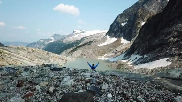 不列颠哥伦比亚省美丽的落基山脉冰川冰湖瀑布附近的白种人青年徒步旅行者空中景观 — 图库视频影像