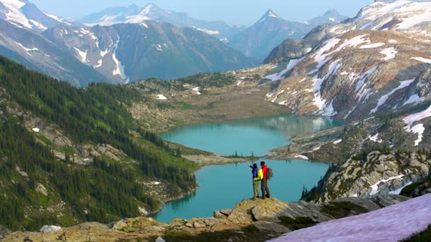 レイクビューHeliハイカー男性若い白人女性氷河湖カナダの近くの風光明媚な山の中を歩くハイキング — ストック動画