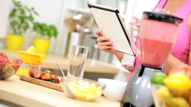 Дівчина на кухні використовує планшет і блендер — стокове відео