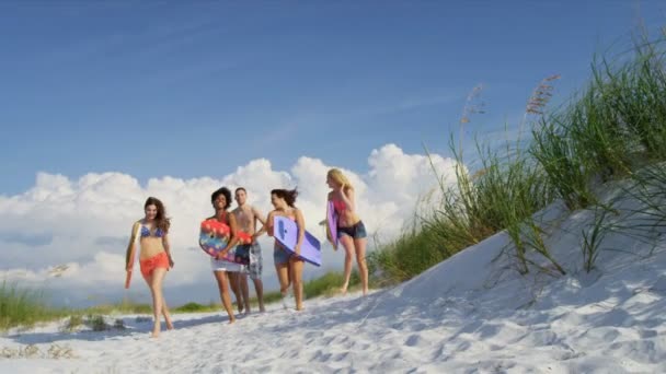 Adolescentes carregando pranchas de corpo em toda a praia — Vídeo de Stock