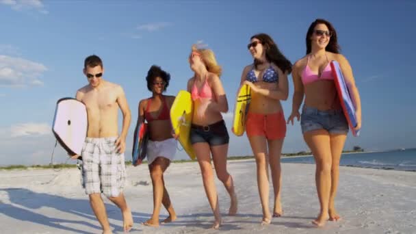 Подростки несут доски для тела по всему пляжу — стоковое видео