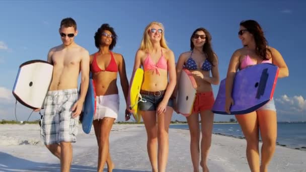 Teenagers carrying body boards across beach — Stock Video