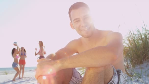 Teenager sitting on beach while friends play ball — Stock Video